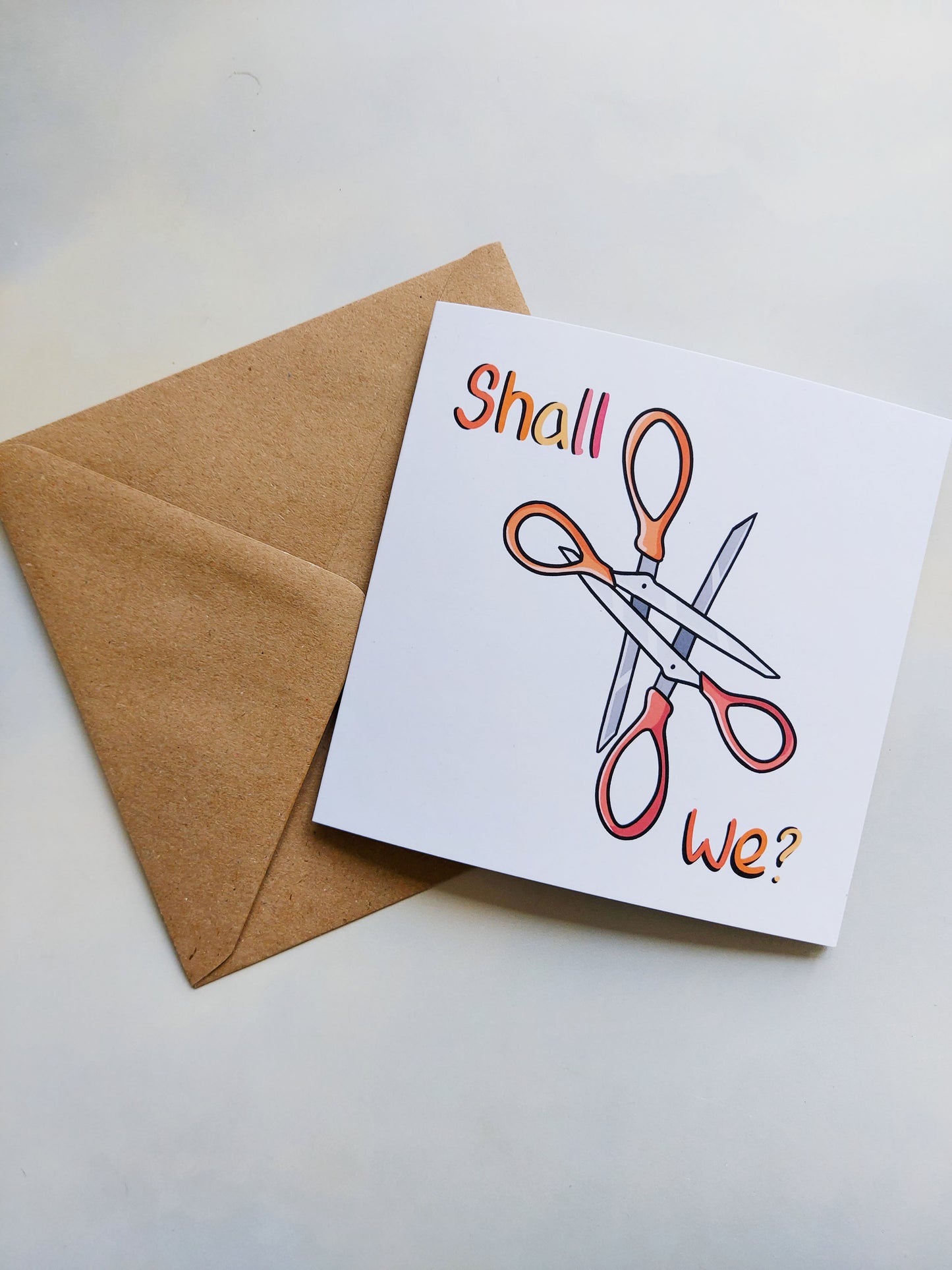 Shall We Scissor? • Funny Lesbian Greeting Card - EmilsDoodles
A greeting card with a kraft envelope. On the card are two interlocking scissors, with the phrase: Shall we? Which is in the lesbian pride flag colours.