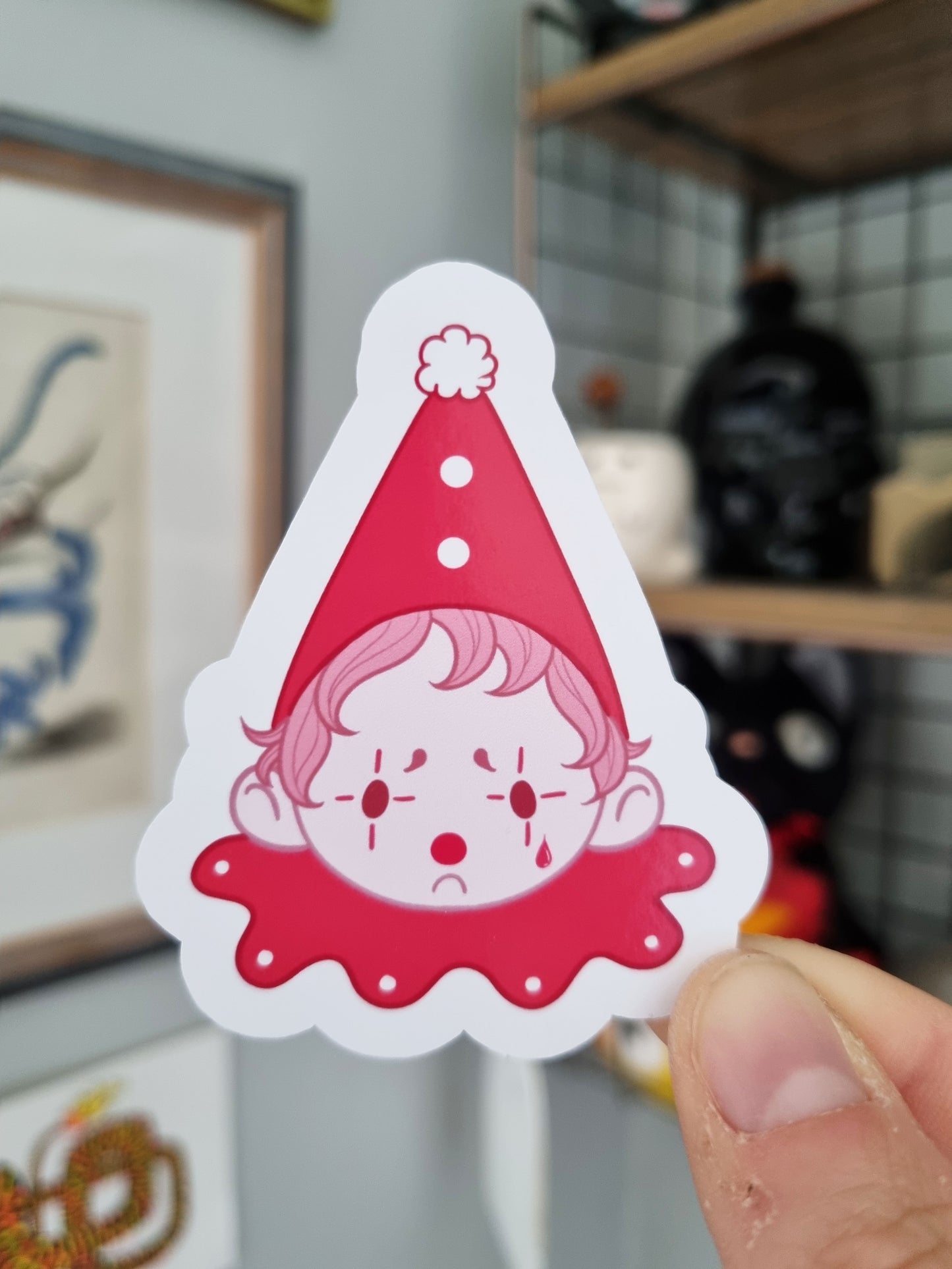 The Sad Clown | Glossy Clown Sticker - EmilsDoodles
A hand holds a glossy sticker of a sad clown. It's pink monochrome. With a dark pink hat and ruffle.