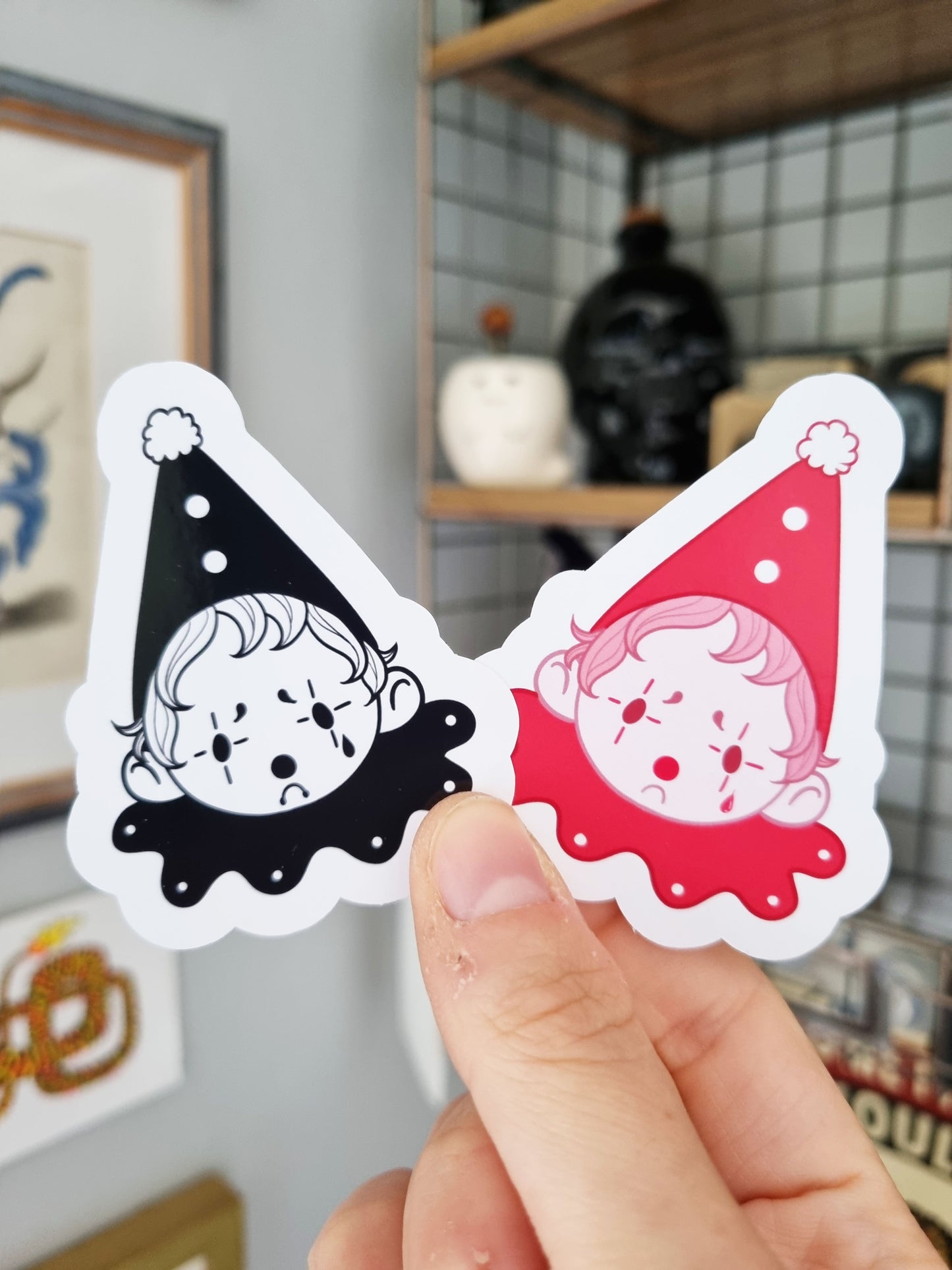 The Sad Clown | Glossy Clown Sticker - EmilsDoodles
A hand holds two sad clown stickers. One is black and white, and the other is pink monochrome.