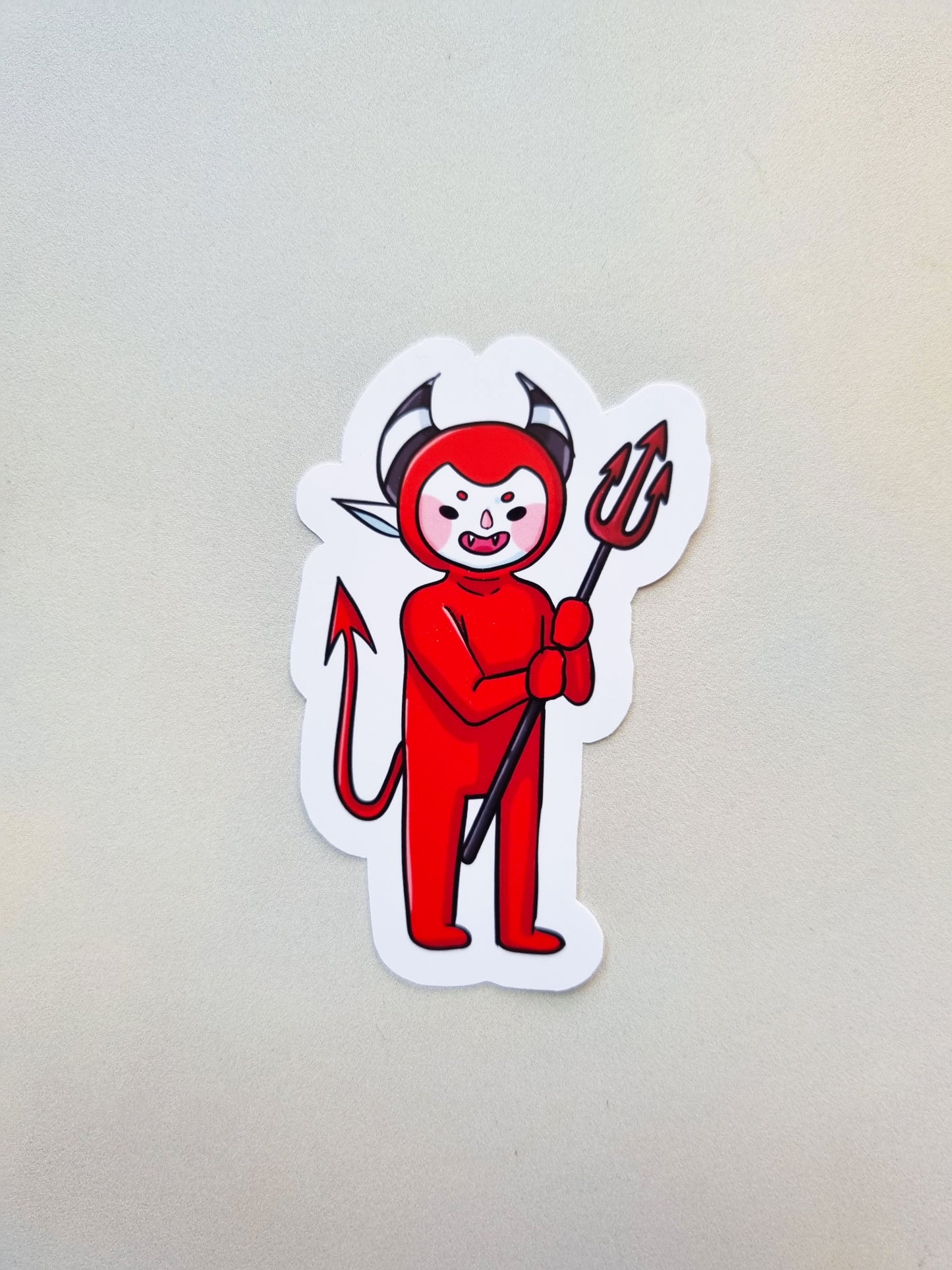 Sticker of a red devil character with horns and a pitchfork on a light gray background