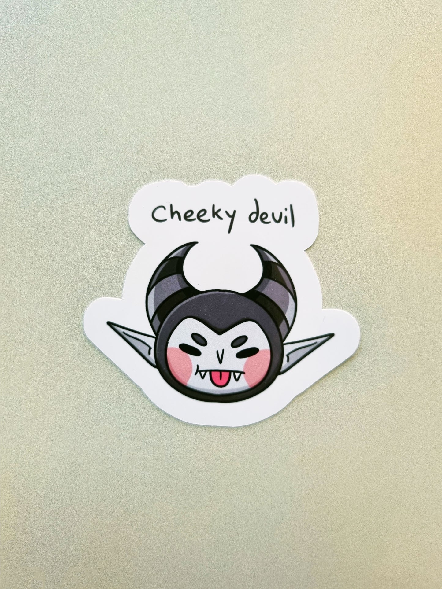 Sticker of a grey devil with horns and blush cheeks, with the phrase "cheeky devil" above it.