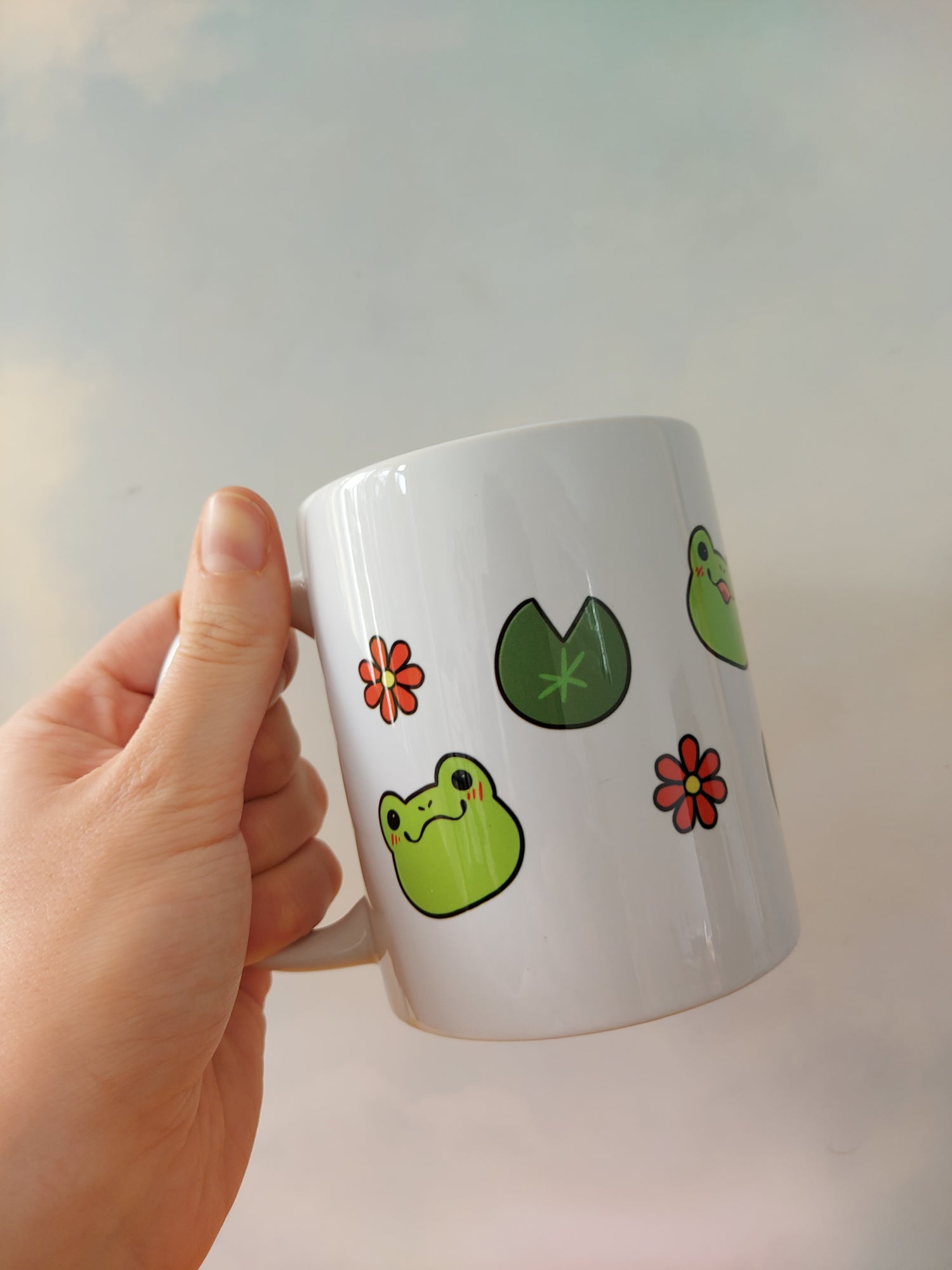 Emotions of a Frog 11oz Mug - EmilsDoodles

A hand holding a mug. On the mug are frogs, flowers, and lily pads. Each frog face has a different emotion. They're also drawn in a kawaii art style.
