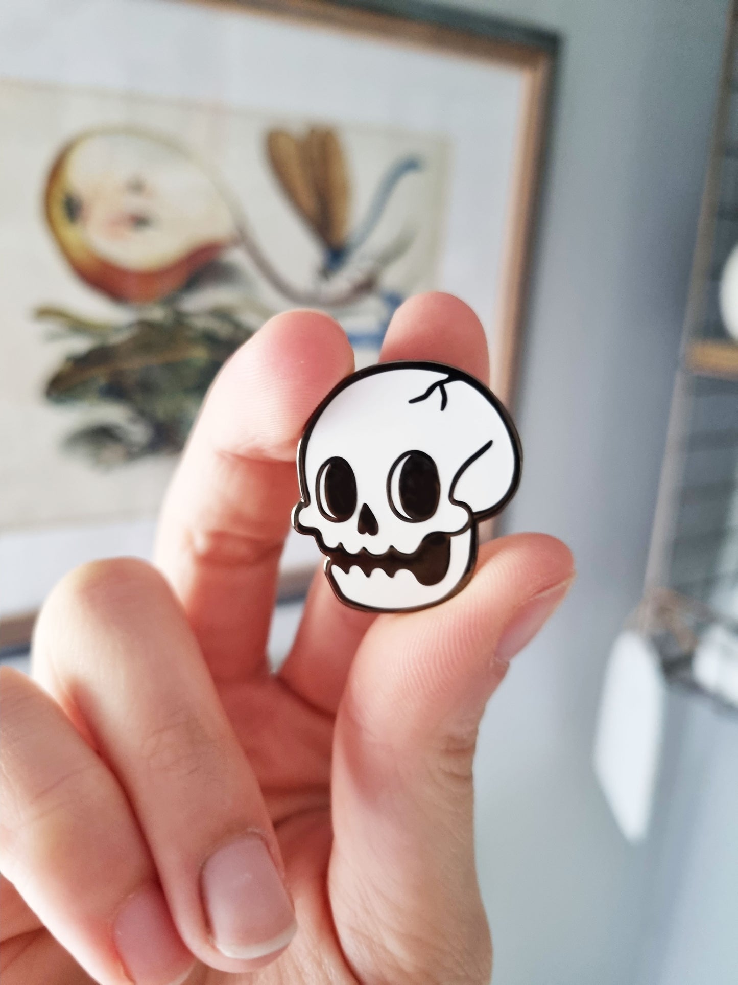 Being held between the thumb, pointer and middle finger is a cartoony skull pin. 