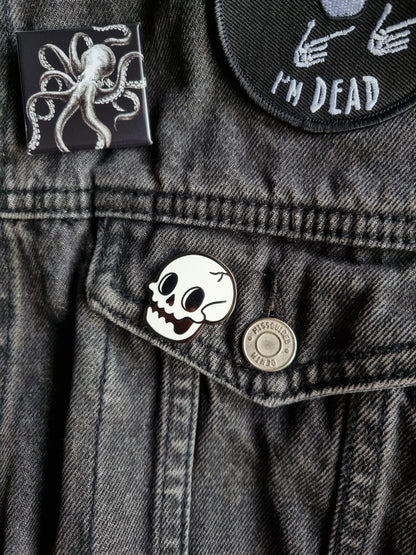 A cartoony black and white skull pin is pinned onto a black denim jacket.