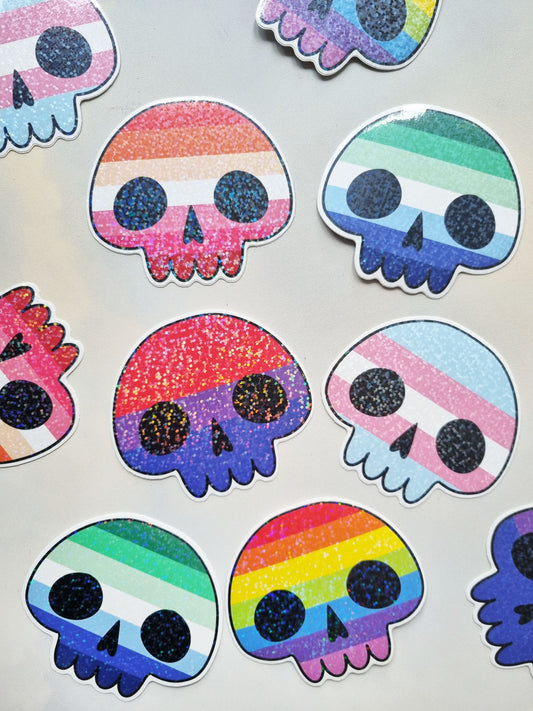 On a light background several stickers are laid. The stickers are holographic and in the shape of a skull, inside are LGBT pride flags: Lesbian, gay, bisexual, transgender, and the rainbow pride flag.