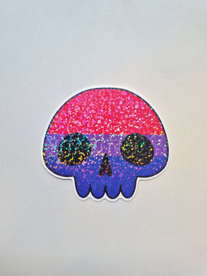 On a light background is a cartoony skull shaped sticker with the bisexual pride flag inside. It has a holographic overlay.