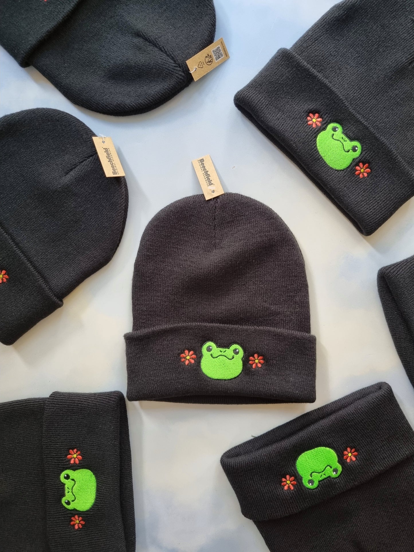 Black beanies with green frog designs on a light blue background