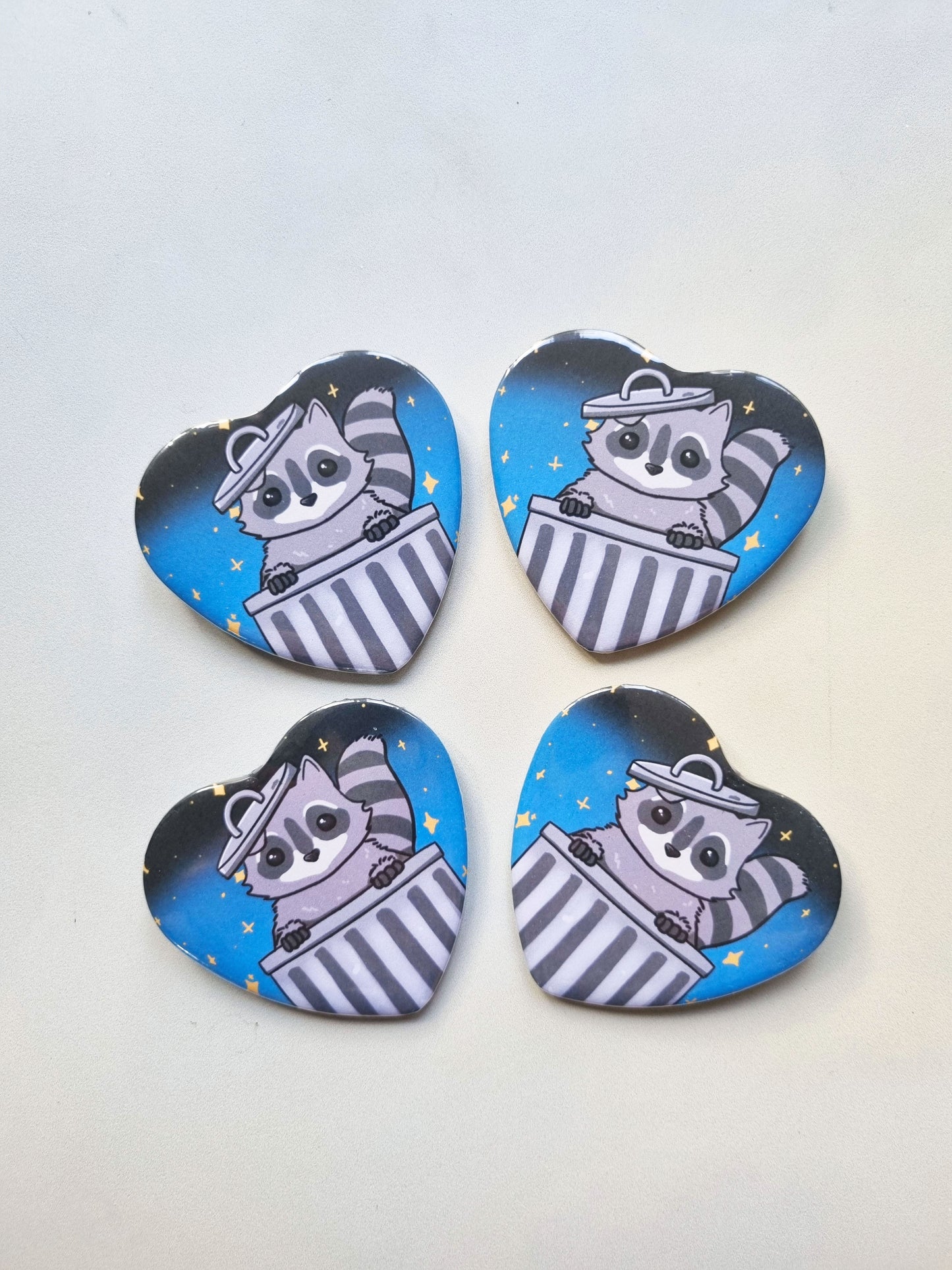 Four heart-shaped buttons with raccoon illustrations on a white background