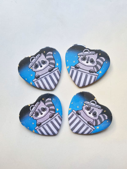 Four heart-shaped buttons with raccoon illustrations on a white background