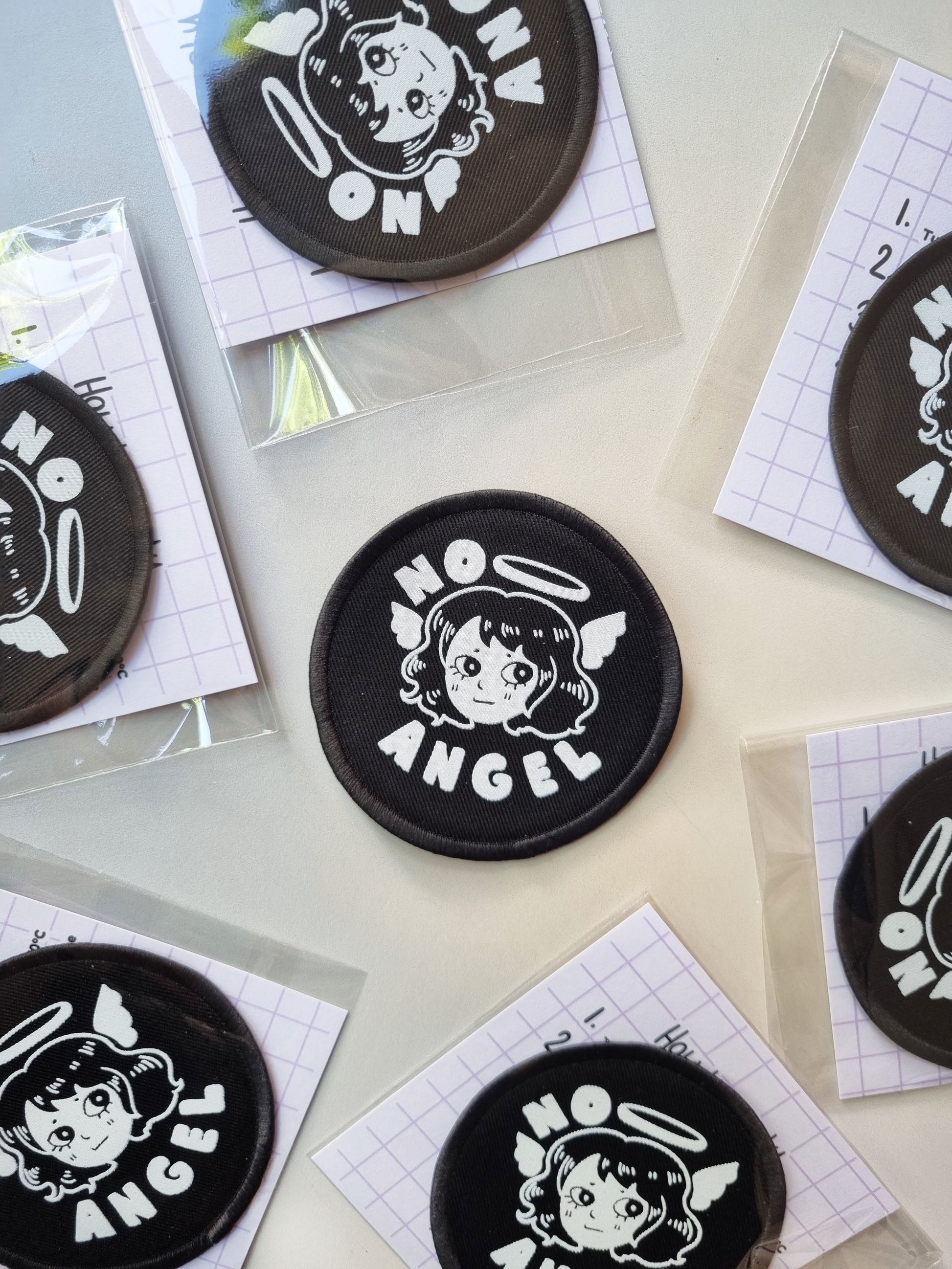 A circler patch with a cute angle design with the text "no angel" on a sky background. 
