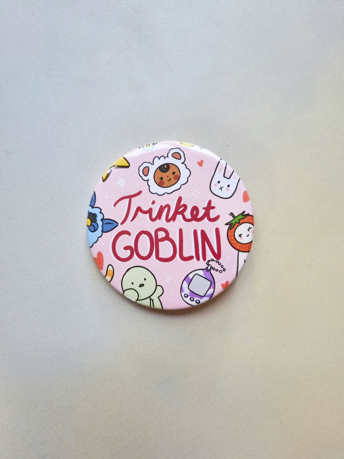 A round pink badge with drawing of cute trinkets, with trinket GOBLIN written in the centre.