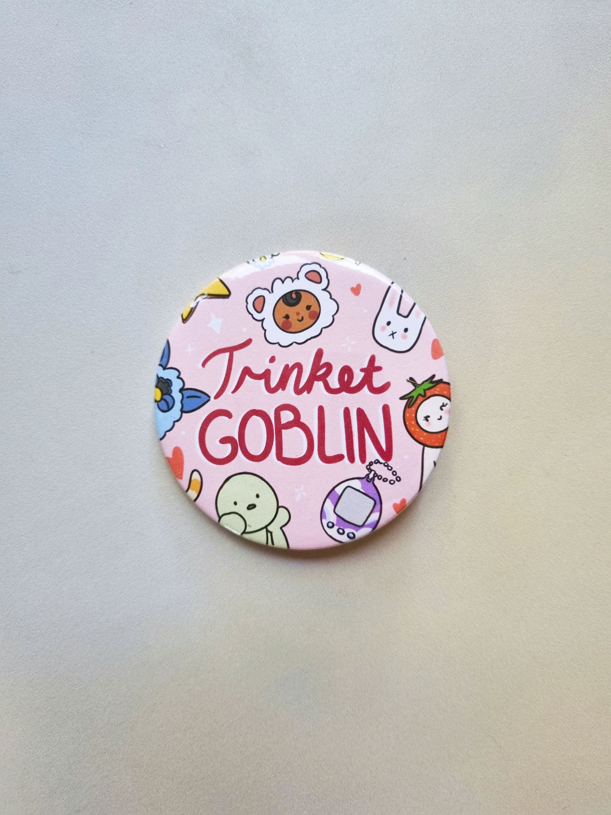 A round pink badge with drawing of cute trinkets, with trinket GOBLIN written in the centre.