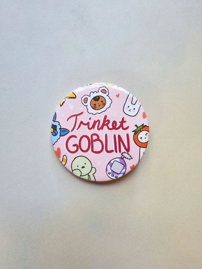 A round pink badge with drawing of cute trinkets, with trinket GOBLIN written in the centre.
