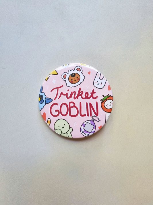 A round pink badge with drawing of cute trinkets, with trinket GOBLIN written in the centre.